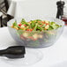 A Carlisle Petal Mist clear polycarbonate bowl filled with salad on a table.