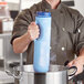 A man in a chef's uniform using a Vollrath Safety Mate Insta Chill Cooling Paddle to chill a blue jug.