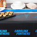 A Creative Converting Carolina Panthers plastic table cover on a table with food and plates.