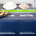 A Seattle Seahawks plastic table cover on a table with plates and cups.