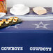 A table with a Creative Converting Dallas Cowboys plastic table cover, plates, and food.