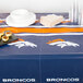 A table with a Denver Broncos tablecloth on it, with plates and cups.