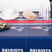 A New England Patriots plastic table cover on a table with plates and cups.