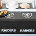 A table with a Las Vegas Raiders table cover on it with food and drinks.