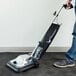 A person using a Lavex upright bagged vacuum cleaner to clean the floor in a professional kitchen.