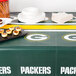 A Creative Converting Green Bay Packers plastic table cover on a table with plates and snacks.