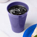 A purple Creative Converting plastic cup with ice next to a sandwich.