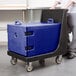 A man pushing a blue Cambro insulated tray carrier on a black cart.