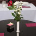 An American Metalcraft stainless steel bud vase with flowers on a table.