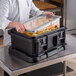 A person using a Cambro top loading food pan carrier to hold food.