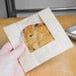 A hand holding a chocolate chip cookie in a Bagcraft Packaging EcoCraft paper bag with a window.