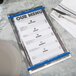 A Menu Solutions Alumitique menu board with Royal Blue bands on a table with silverware on a napkin.