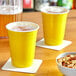 Two yellow Choice plastic cups of beer on a table with mixed nuts.