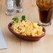 An oval Tuxton china baker filled with macaroni and cheese on a table.