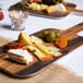 An American Metalcraft rectangular melamine serving peel with cheese, olives, and other food on a faux acacia surface.