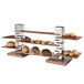 A Rosseto stainless steel multi-level riser with a walnut base holding a display of pastries and muffins.