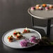 A white Rosseto melamine round tray with pastries and flowers on it on a table.