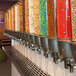 A row of Rosseto topping/candy dispensers filled with different colored candies.