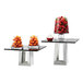 A glass table with two stainless steel pyramid risers holding glass jars of oranges.