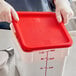 A person in gloves holding a red Choice polypropylene food storage container lid.