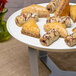 A white round tray with pastries on a table with a 3-leg silver riser.
