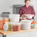 A woman in a chef's uniform uses a white Choice food storage container in a kitchen.