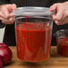 A hand holding a Choice clear round polycarbonate food storage container filled with red liquid.