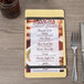 A Menu Solutions natural wood menu board with rubber band straps on a table with a fork and knife.