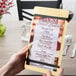 A hand holding a customizable wood menu board with rubber band straps.