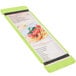 A lime green wood menu board with rubber band straps holding a menu with a picture of spaghetti.