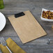 A Menu Solutions weathered walnut wood clipboard holding a plate of nuts with a fork on a table.
