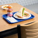 A blue plastic fast food tray with a sandwich, drink, and napkin on a table.