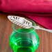 A Franmara stainless steel absinthe spoon with a sugar cube on top of a glass of green liquid.