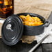 A black Libbey mini cast iron oval dutch oven with food in it and a lid on a table.
