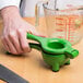 A hand using a green Tablecraft lime juicer to make a drink.