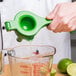 A person using a Tablecraft lime juicer to squeeze lime juice into a measuring cup.