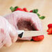 A person in plastic gloves using a Mercer Millennia paring knife to cut a strawberry.