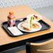 A black plastic fast food tray with a sandwich and a bowl of fruit on it.