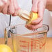A person using a Franmara beechwood citrus reamer to juice a lemon into a measuring cup.