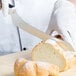 A person wearing white gloves uses a Mercer Culinary Millennia bread knife to cut a loaf of bread.