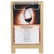 A Menu Solutions natural wood sandwich menu board tent with a clip holding a menu on a wood stand on a table with a glass of red wine.