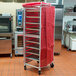 A red Curtron Supro mesh rack cover on a bun pan rack with trays.