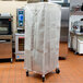 A large white Curtron breathable mesh cover on a metal bun pan rack.