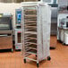 A gray Curtron Supro bun pan rack cover on a large metal rack in a kitchen.