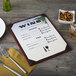 A customizable mahogany wood menu board with picture corners on a table with a fork and knife.