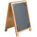 A Menu Solutions Country Oak wooden table tent with black picture corners and a black board on it.