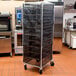 A black Curtron Supro bun pan rack cover on a large metal rack with trays in a kitchen.