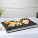 A Vollrath reversible display platter with cheese and grapes on a table.