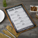 A Menu Solutions country oak wood menu board on a table with a fork and knife.