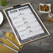 A Menu Solutions wood menu clip board on a table with silver utensils and a yellow cloth.